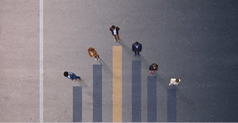 An overhead shot of a group of people shows them each standing at the pinnacle of a bar graph etched into the floor.