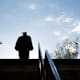 Silhouette of a college graduate in a cap and gown climbing up a set of steps on a university campus.
