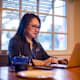 Asian American female business student in her mid-40s typing an assignment for her online class at home. She is sitting at her dining room table, and is wearing glasses and business casual clothes.