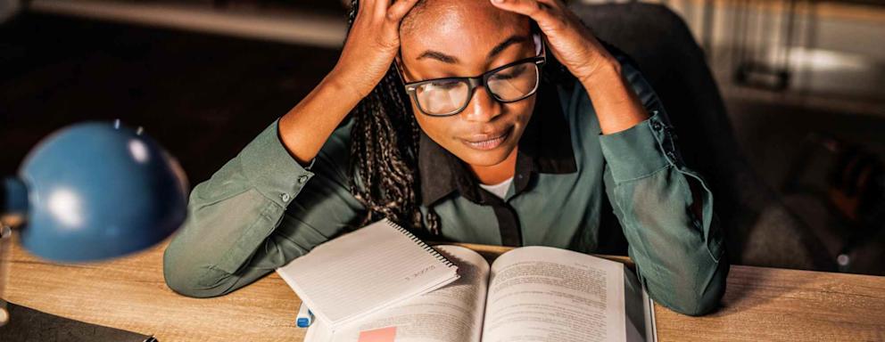 Tired female student reading a book, holding head in hands