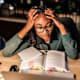 Tired female student reading a book, holding head in hands