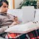 College student lying on a couch in his living room paying his student loan bill online with his credit card.